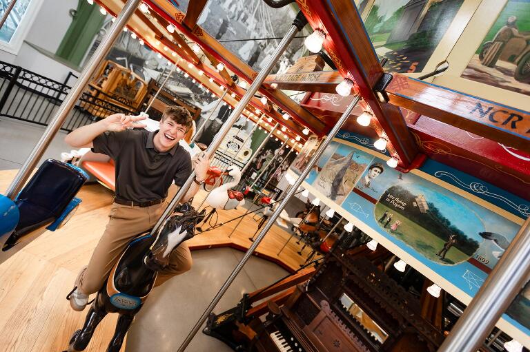 Smiling senior guy giving a peace sign while riding a carousel horse at Carillon Historical Park.
